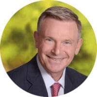 Dudley Poppens, Senior Vice President of Sales for Compass Healthcare wearing a black suit and red tie against a blurred green background