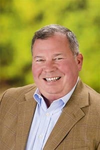 Smiling man in tan blazer on blurred green background
