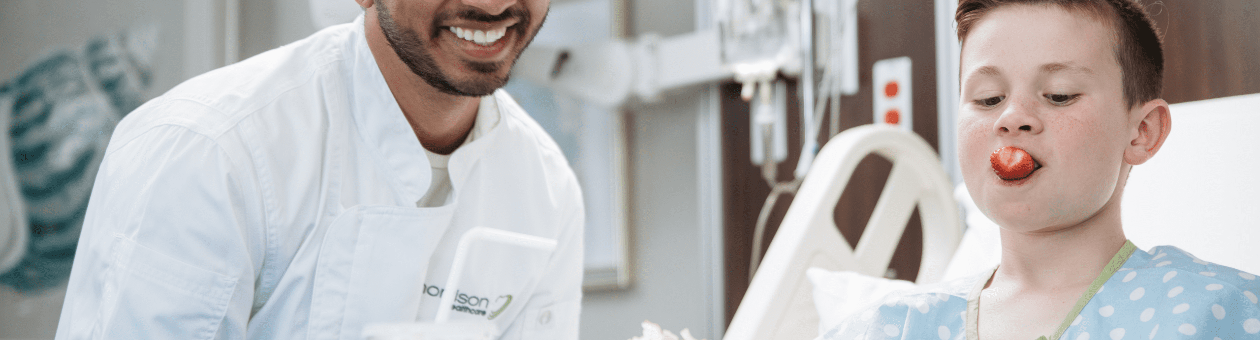Smiling doctor with young patient eating a tomato in hospital hallway