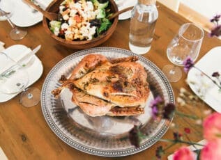 Roasted chicken on silver platter with salad on wooden table set for dinner