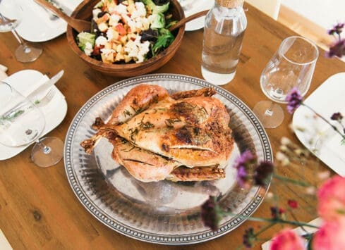 Roasted chicken on silver platter with salad on wooden table set for dinner