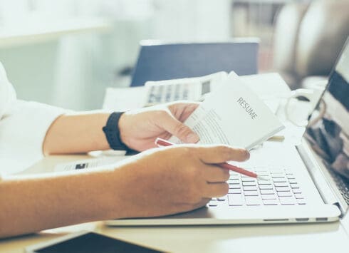 Hands holding resume at laptop keyboard during job application process