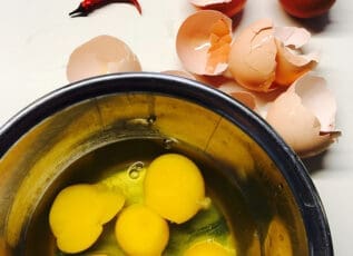 Cracked eggs in bowl next to eggshells and chili peppers for Morrison Healthcare recipe