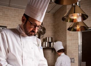 Chef preparing food in a professional kitchen with assistant in background