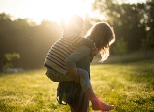 Young boy carrying girl piggyback in sunny park at sunset