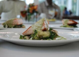 Salmon filet with greens on white plate, fine dining restaurant setting in background