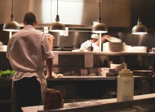 Chefs preparing meals in a busy restaurant kitchen with stainless steel equipment and pendant lights