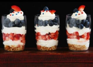 Patriotic parfaits with fresh berries, whipped cream, and blueberries in clear glasses on wooden surface