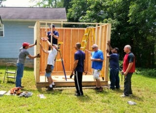 Group of volunteers building wooden structure in backyard