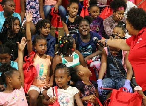 Group of smiling and waving African American children wearing colorful clothing, holding gift bags