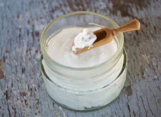 Creamy coconut oil body scrub in glass jar with wooden scoop on rustic wooden surface