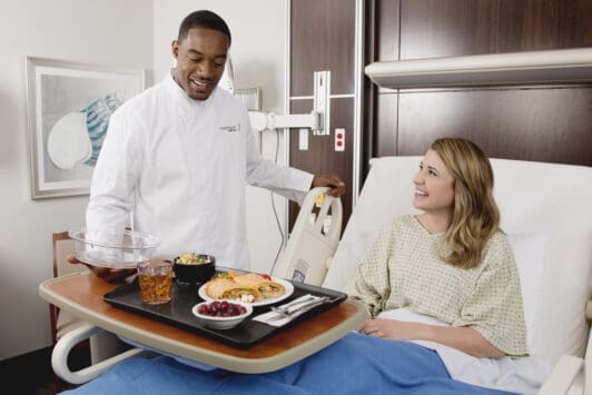 Morrison Healthcare associate serving patient meal in hospital room