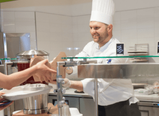 Chef in white uniform smiling while preparing food in commercial kitchen