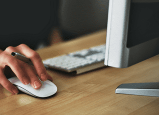 Woman's hand using computer mouse on wooden desk with keyboard in background
