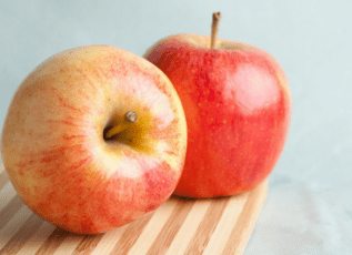 Two fresh red and yellow apples on a wooden cutting board, one with a visible stem