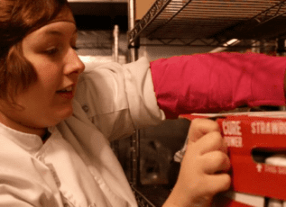 Employee stocking strawberry milk in refrigerated section of commercial kitchen