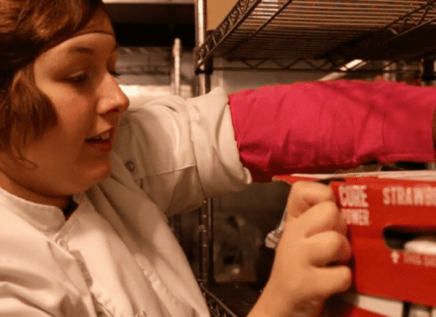 Employee stocking strawberry milk in refrigerated section of commercial kitchen