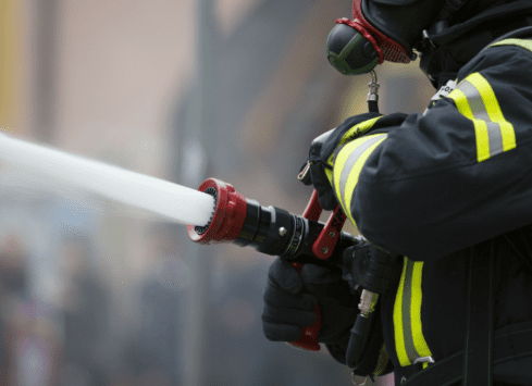 Firefighter spraying water from fire hose to extinguish fire