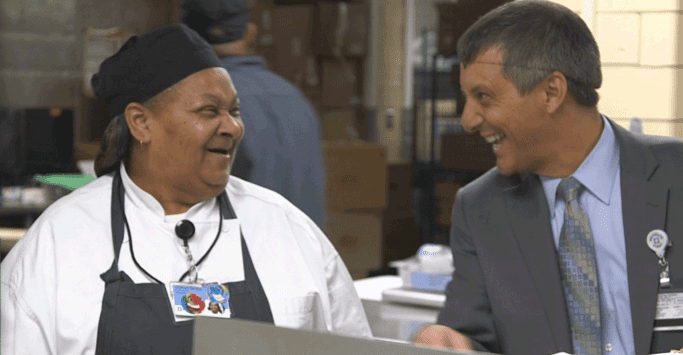 Two smiling Morrison Healthcare employees standing together in a kitchen wearing chef uniforms