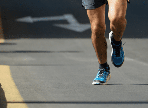Close-up of man's legs running on road in blue athletic shoes