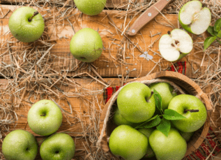 Fresh green apples on a wooden cutting board with straw and leaves
