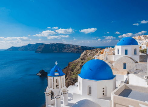 Blue domed churches overlooking the Aegean Sea in Oia, Santorini, Greece on a sunny day