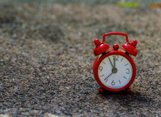 Red vintage alarm clock on gravel showing 12 o'clock