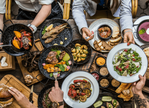 Healthy restaurant meal spread with salads, vegetables, grilled meats, and sides on rustic table