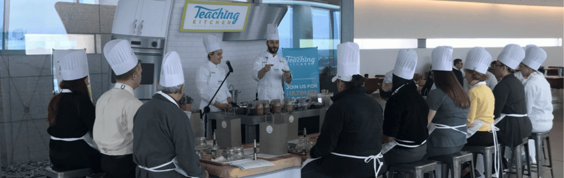 Teaching Kitchen cooking demonstration with male chef instructing group of students in chef hats
