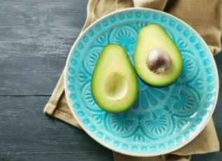 Avocado halves on teal decorative plate on dark wooden surface with brown cloth napkin