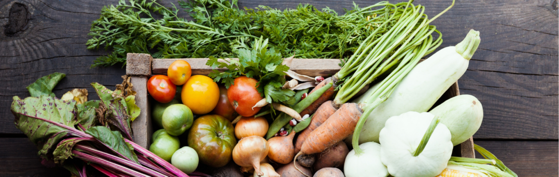Variety of fresh vegetables and herbs in wooden crate on rustic table