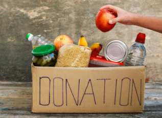 Hand picking an apple from donation box filled with non-perishable food and fresh produce