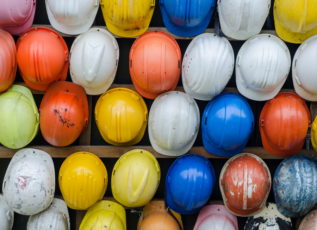 Colorful construction hard hats hanging on wall, featuring yellow, white, orange, red and blue helmets