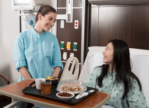 Patient smiling at nurse serving meal in hospital room