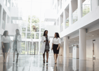 Two businesswomen walking and talking in a modern office building with floor-to-ceiling windows