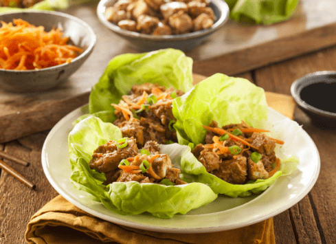 Asian lettuce wraps with chopped chicken, carrots and soy sauce on rustic wooden table