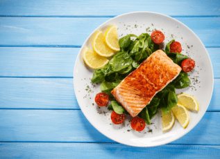 Grilled salmon with spinach salad, cherry tomatoes, and lemon on a white plate
