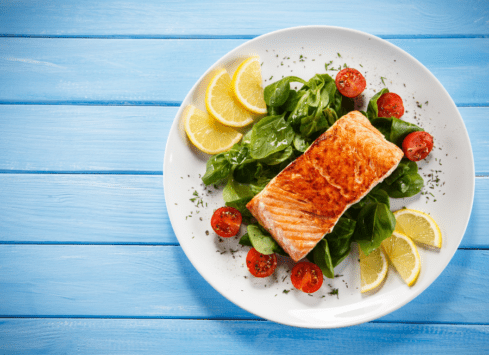 Grilled salmon with spinach salad, cherry tomatoes, and lemon on a white plate
