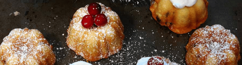 Holiday bundt cakes topped with powdered sugar and cranberries on a dark surface
