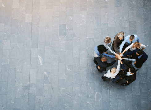 Business people joining hands in circle on tile floor, viewed from above
