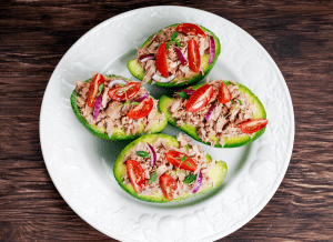 Tuna salad stuffed avocado boats with tomatoes and red onions on a white plate