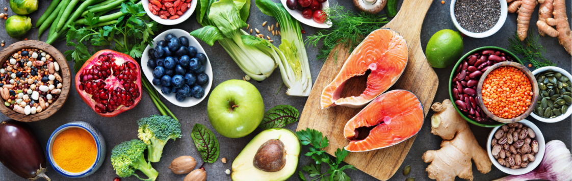 Colorful healthy foods including fruits, vegetables, fish, nuts, seeds and spices arranged together