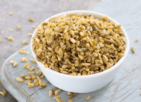 Organic freekeh grain in white bowl on rustic wooden surface with scattered grains
