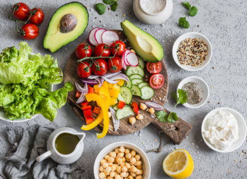 Healthy salad ingredients on rustic wood board including fresh vegetables, chickpeas, avocado and herbs