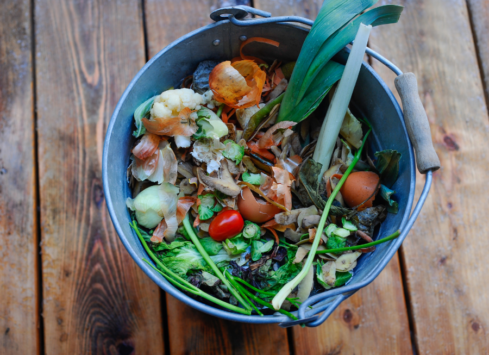 Vegetable food scraps in compost bin on wooden table