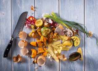 Knife cutting assortment of food waste scraps on wooden table for composting