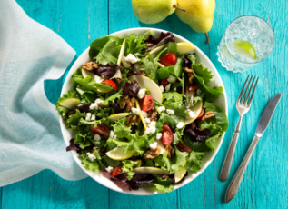 Pear salad with mixed greens, tomatoes, feta cheese, and walnuts on teal wooden table