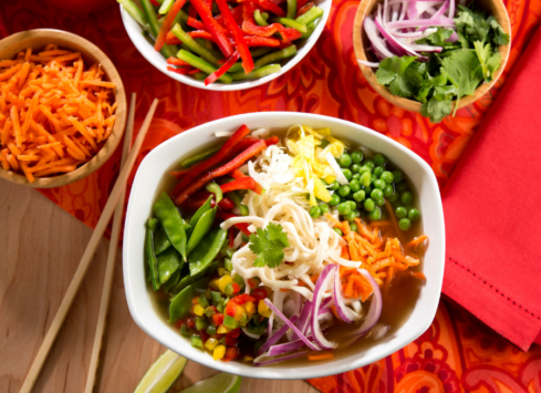 Colorful vegetarian pho bowl with noodles, vegetables, herbs served on vibrant red tablecloth