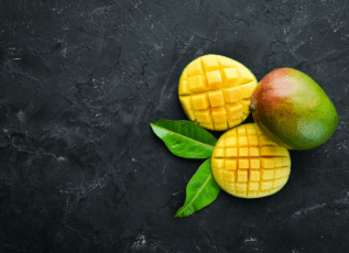 Sliced mango fruit with leaves on dark stone background