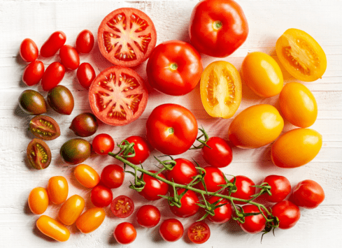 Cherry tomatoes in various colors with sliced tomatoes on a white wooden surface